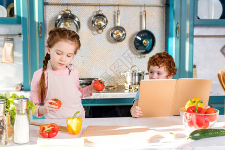 孩子们带着食谱和蔬菜一起在厨房做饭图片
