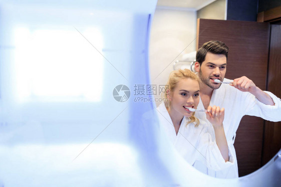 微笑的情侣刷牙在浴室里照镜子图片