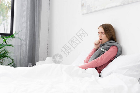 家里有咳嗽的生病女孩在床上与温度计图片