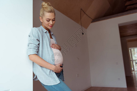 美丽的女孩手放在怀孕的肚子上站在墙边图片