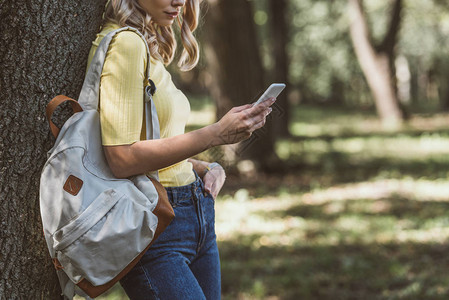 在森林里用智能手机对肩背着包的妇女图片