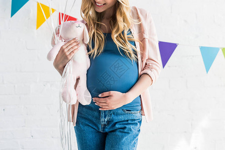 孕妇触摸肚子和在婴儿聚会上持有玩具的作物形象图片