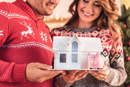 一对夫妇在圣诞节毛衣中持有房屋模型和小猪银图片