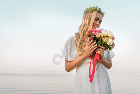 穿着白裙子和花圈的笑着迷人的新娘看着海滩图片