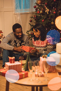 在家里庆祝圣诞节时向女朋友赠送礼物的非洲男人微笑着图片