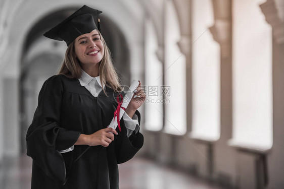 穿着学术服装的漂亮年轻女毕业生拿着文凭图片