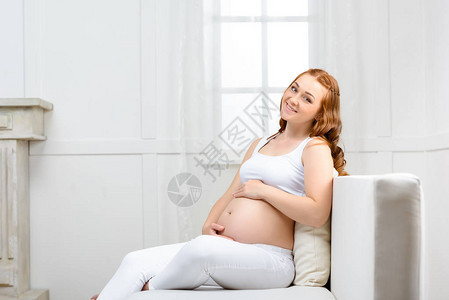 微笑着的美丽的孕妇触摸她的肚子看着图片