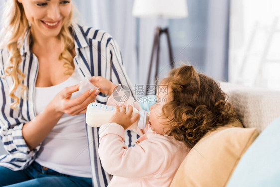 在家里用瓶子喂着可爱的婴儿女婴时笑着微笑的母亲图片