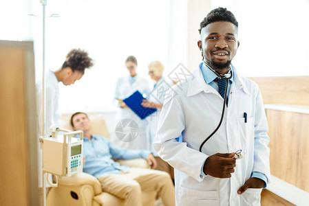 身穿实验室大衣的年轻非洲美国青年医生与同事和背景男病人站在一起图片