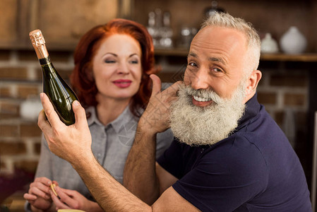 有选择焦点微笑的老年男子手拿着一瓶酒看着镜头和妻子坐在图片