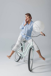 带着白色气球坐在自行车上的快乐的迷人女孩图片