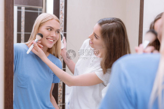 女孩用化妆刷在朋友脸上涂粉底图片