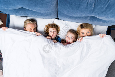 有两个孩子躺在毯子下躺在床上的图片