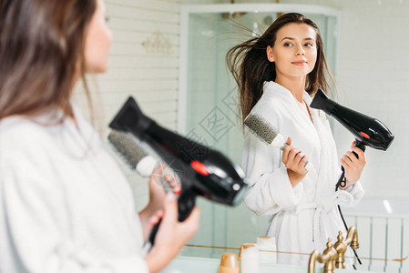 在浴室照镜子时拿着梳子和干头发的年轻美图片