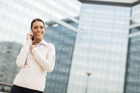 在办公大楼前用移动电话说的年轻商业女图片