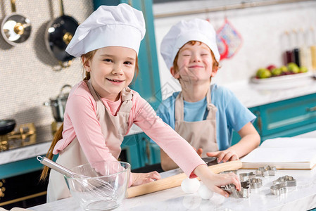 穿着厨帽和围裙的可爱小可爱小孩在厨房一起做饭时图片