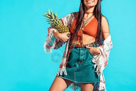 在绿松石上拿着菠萝的微笑波西米亚女孩的裁剪图像图片