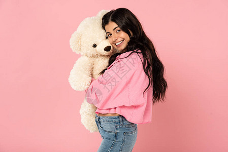 微笑的女孩拥抱泰迪熊被粉红色隔离图片