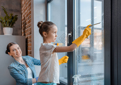 快乐的母亲和可爱的小女儿在保护手套清洗窗口一起图片