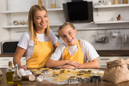 身穿围裙的幸福母亲和女儿准备饼干在厨图片