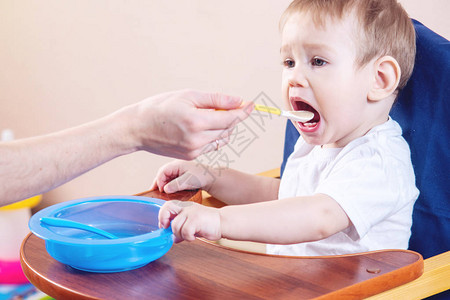 可爱的小男孩坐在厨房的椅子上吃着张大嘴巴妈手里图片
