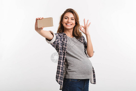 年轻快乐的怀孕少女用智能手机自拍图片