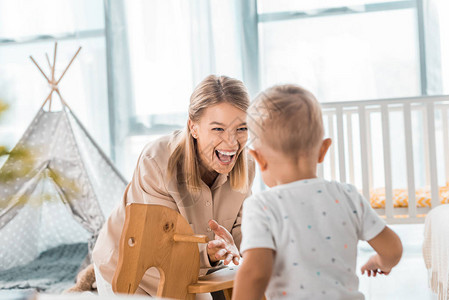 快乐的母亲和幼儿在育婴室玩具木制图片