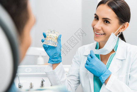带着牙套给病人展示牙科下巴模型的微笑女图片