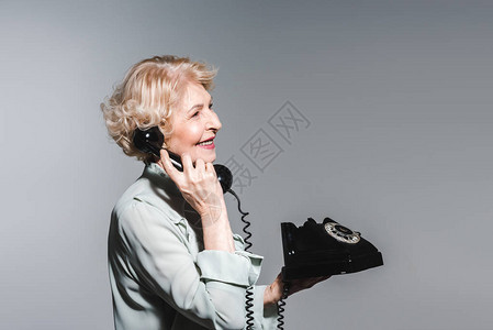 一面笑着的老女人一边用古老的电话说图片