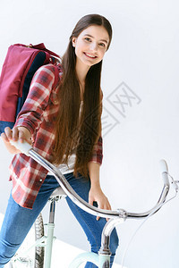 带着背包坐在单车上孤立在白边的年轻女图片