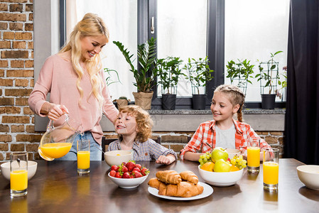 快乐的母亲倒橘子汁让孩子们在家吃早图片