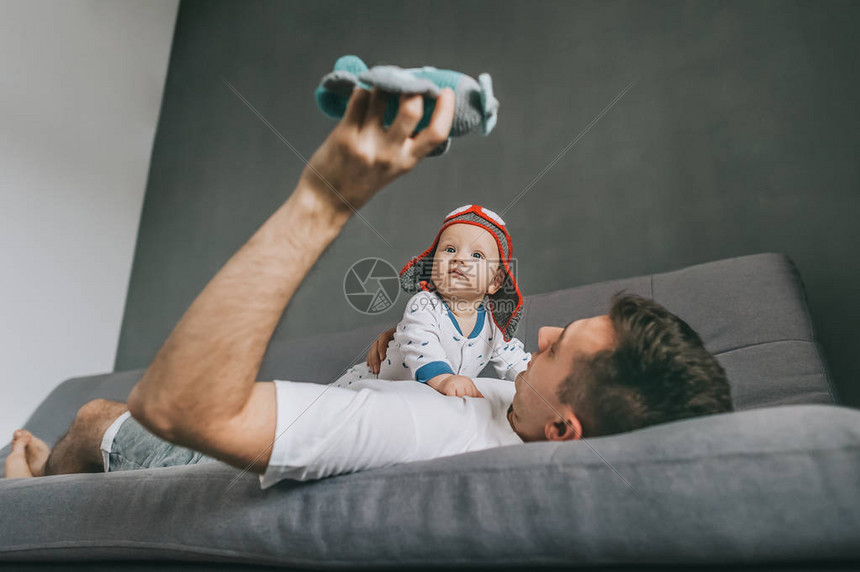 父亲拿着玩具飞机躺在沙发上和戴着针织飞行员帽的图片