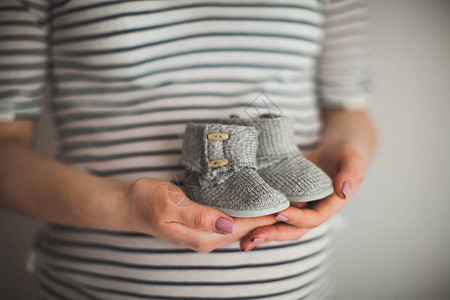 一只手拿着一双小鞋子这是灰色背景的婴儿鞋母婴主题怀孕背景图片