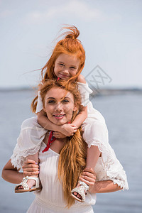 带着可爱的红发女儿在海边脖子上笑图片