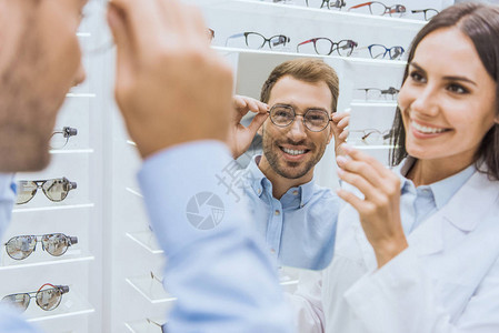 快乐的女观察家抱着镜子微笑的男人在眼科店里图片