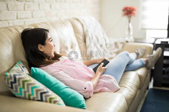 年轻女子躺在舒适的沙发上看电视图片