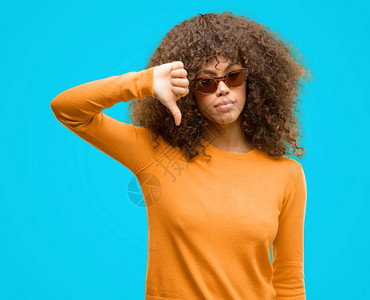 身穿羊毛衫的非裔美国妇女脸色愤怒反面迹象表示不喜欢拇指低下排斥概念背景图片