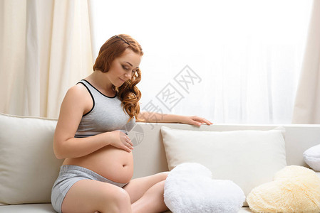 富有吸引力的孕妇在沙发上用心形枕头坐在沙发背景图片