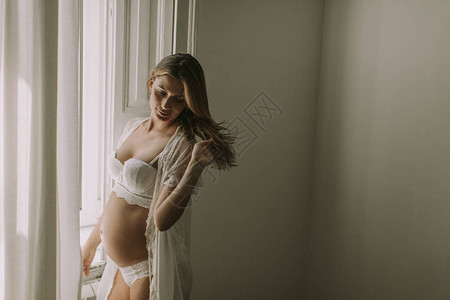 美丽的年轻孕妇站在窗边图片