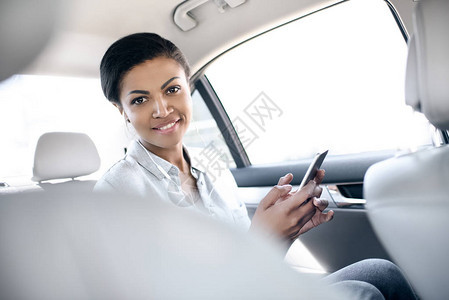 坐在车里并使用智能手机的美丽笑着微背景图片
