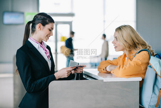 机场工人在报到服务台检查年轻女旅行者证件时微笑的图片