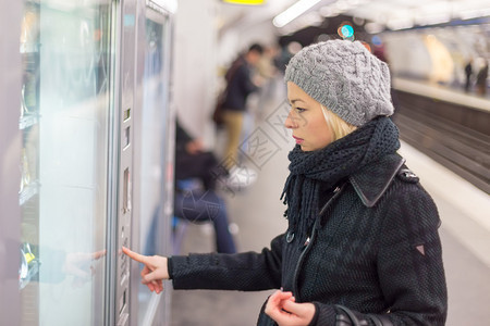 穿着冬大衣的身着临时服装的女人在售票机上买地铁图片