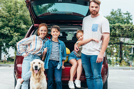 美丽的年轻家庭有狗站在汽车旁图片
