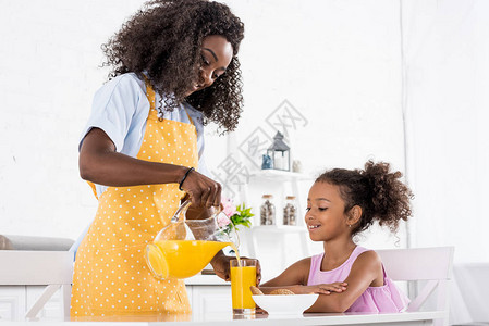 非洲母亲和女儿身着围裙厨房上图片