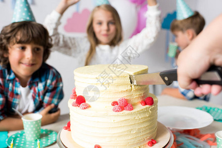 剪手切生日蛋糕和快乐的孩子们站在后图片