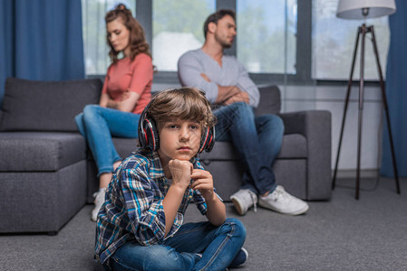 戴耳机的小男孩在坐沙发上辩论的父母时一图片