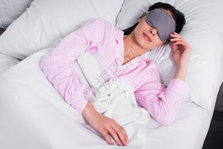 穿着粉红色睡衣和睡着面罩睡在家中床上睡背景图片