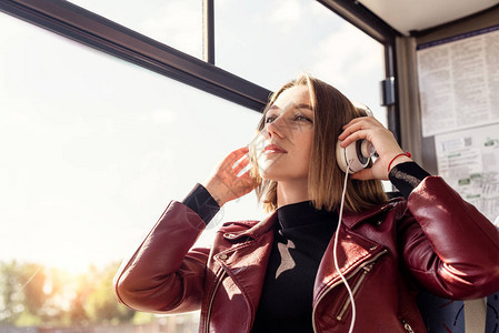 坐在公共交通工具上时用耳机听音乐的年轻有思想的妇女肖像图片