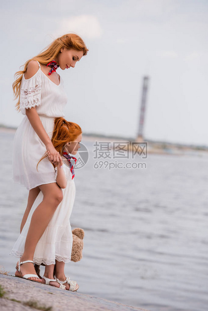 身着白裙子的美丽母亲和女儿在海滨站立图片