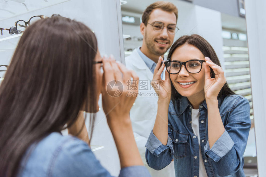 快乐的女人选择眼镜和看镜子的后视图图片